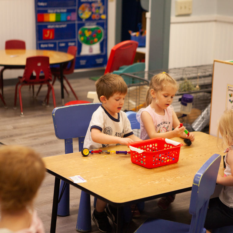 Children playing at a table with toys in a preschool classroom setting.