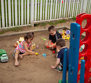 Children playing in sandbox with toys, near a fence at Willow House Preschool.