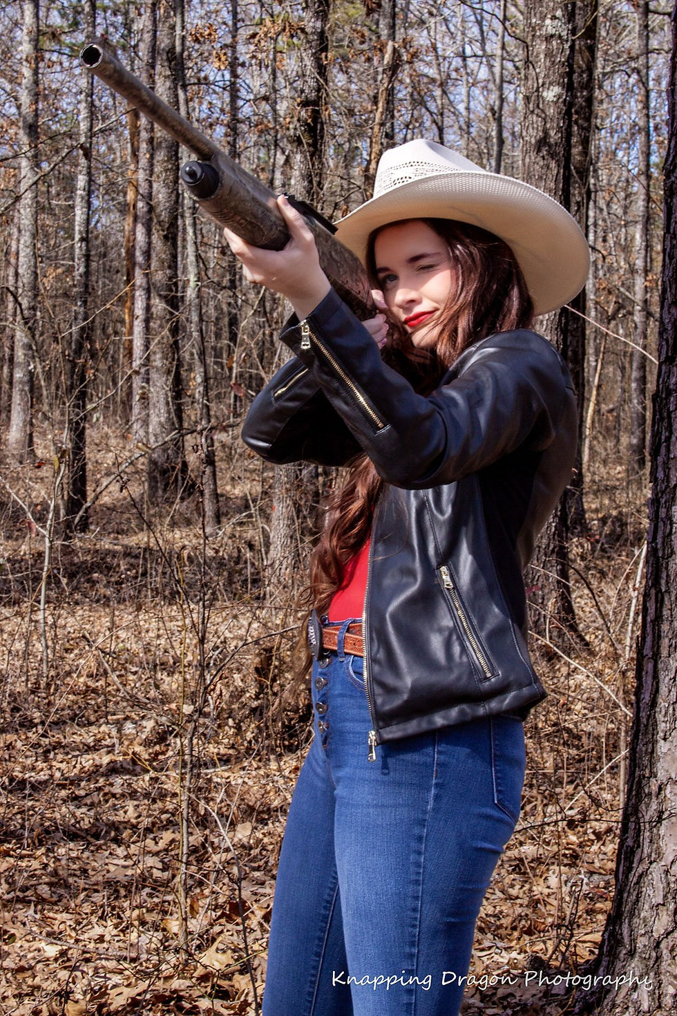 Senior portrait of a Pangburn High School student in Arkansas, holding a rifle with confidence, as she embraces her rural roots in a woodland setting. Photographed by Knapping Dragon Photography.