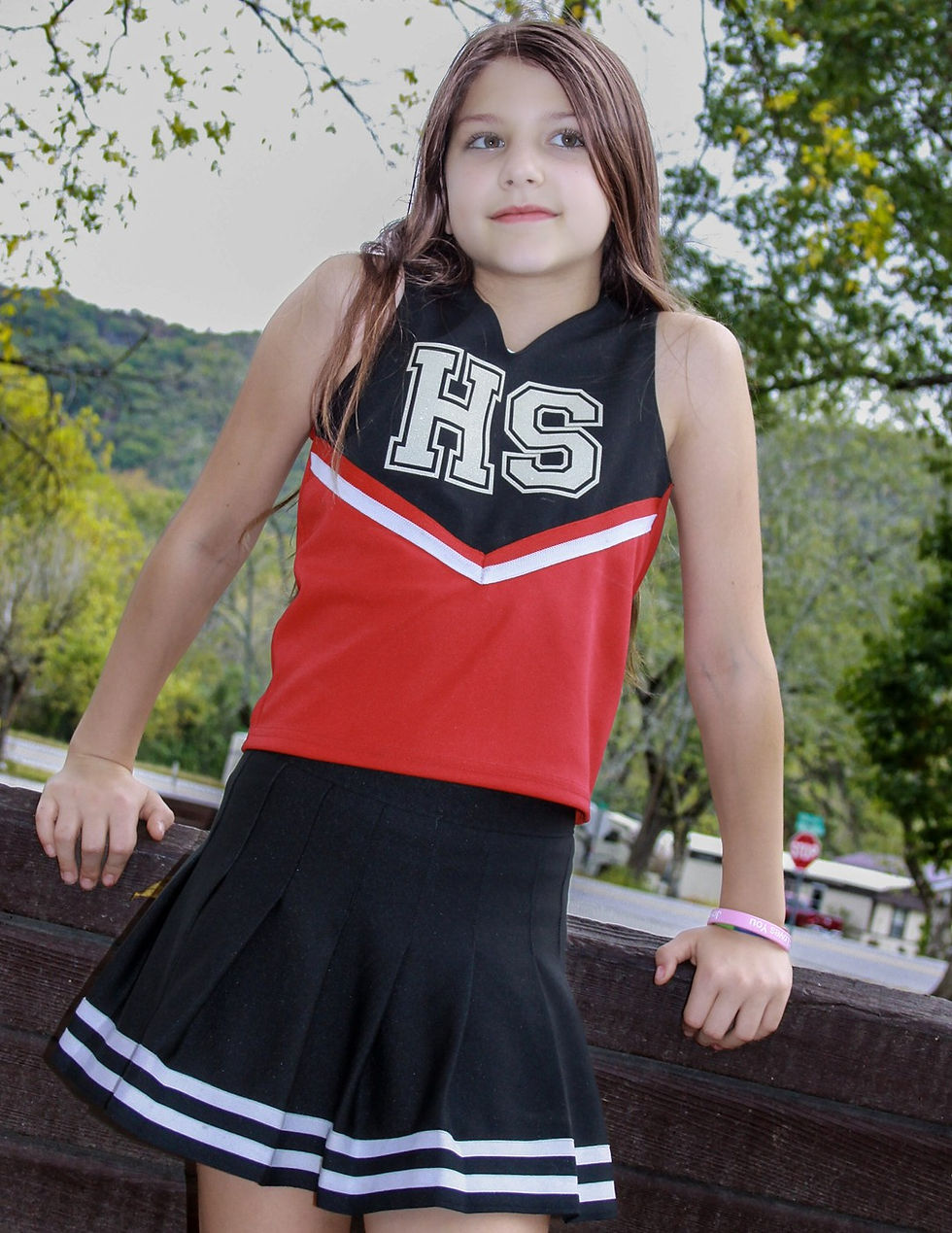 A young cheerleader poses confidently in her red and black uniform, embodying team spirit in a scenic outdoor setting. Captured in the distinctive DragonFire Signature style by Knapping Dragon Photography.