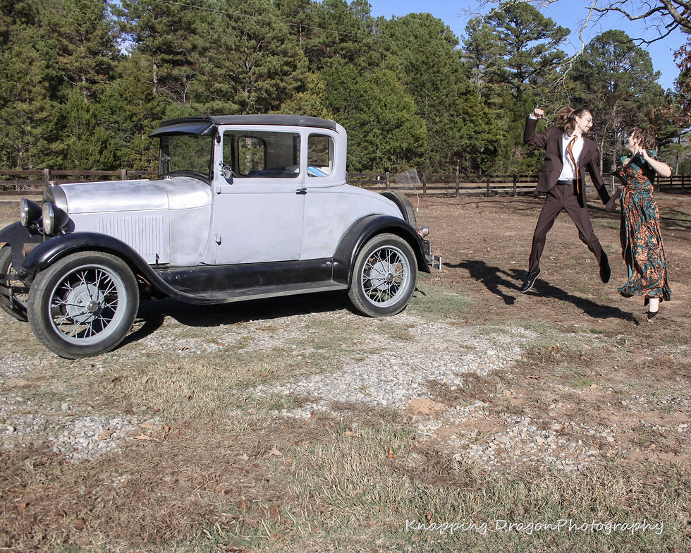 A joyful couple leaps into the air beside a vintage car, celebrating their Thanksgiving wedding in the scenic outdoors of Tumbling Shoals, Arkansas. Captured by Knapping Dragon Photography.