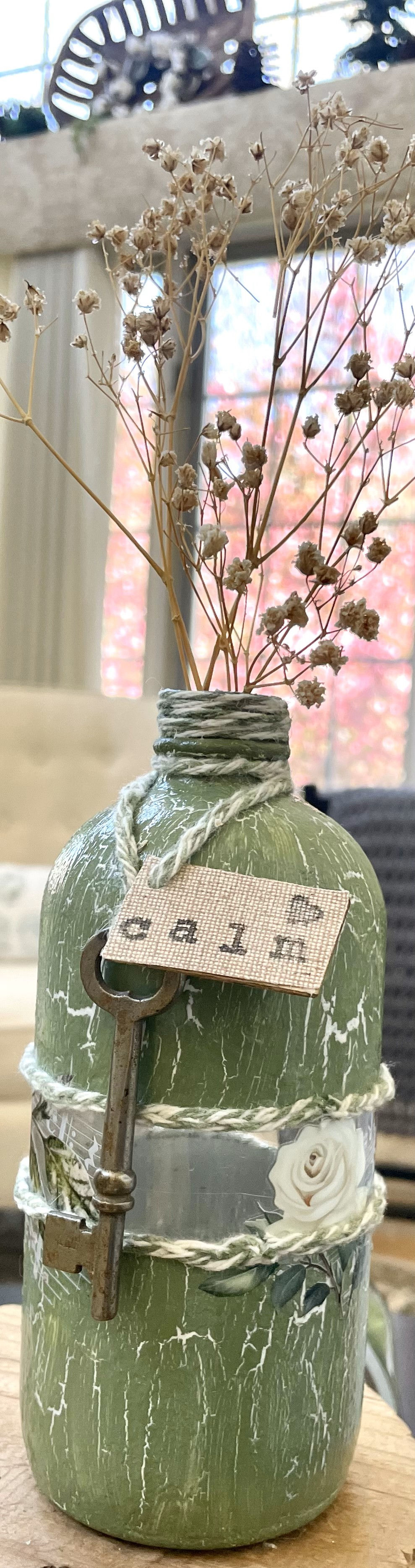 upcycled glass bottle vase in a chippy painted style, embellished with twine, an antique key, wooden heart, and CALM sign