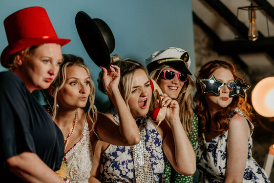 People having fun in photoooth, using props and standing in front of blue backdrop.