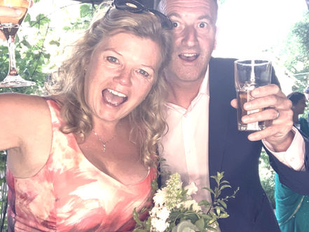 Wedding guest couple (probably mum and dad of bride or groom) raising their glasses in an open barn. Photo booth shot. 