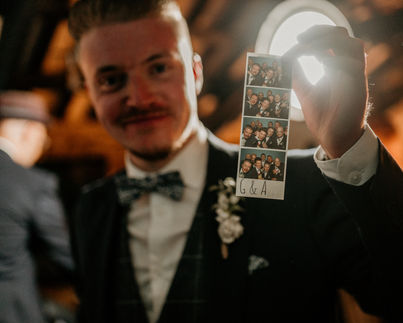 Handsome wedding guest in suit and bow tie showing photo booth print out.