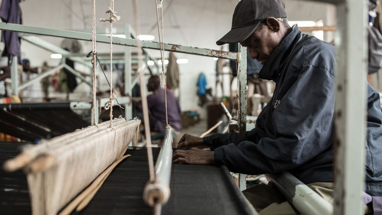 Photo d'un tisseur travaillant sur un métier à tisser artisanal à la manufacture Aïssa Dione, Dakar, Sénégal
