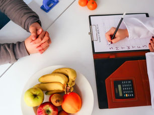 Nutricionista da Ohnutri em BH e paciente numa mesa; ela preenche um plano semanal de refeições, com frutas e calculadora.