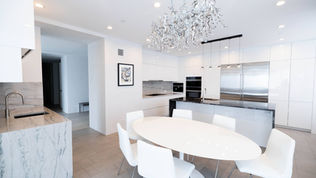 Modern white high-gloss European kitchen with large waterfall marble island, integrated appliances, and L-shaped layout with breakfast bar