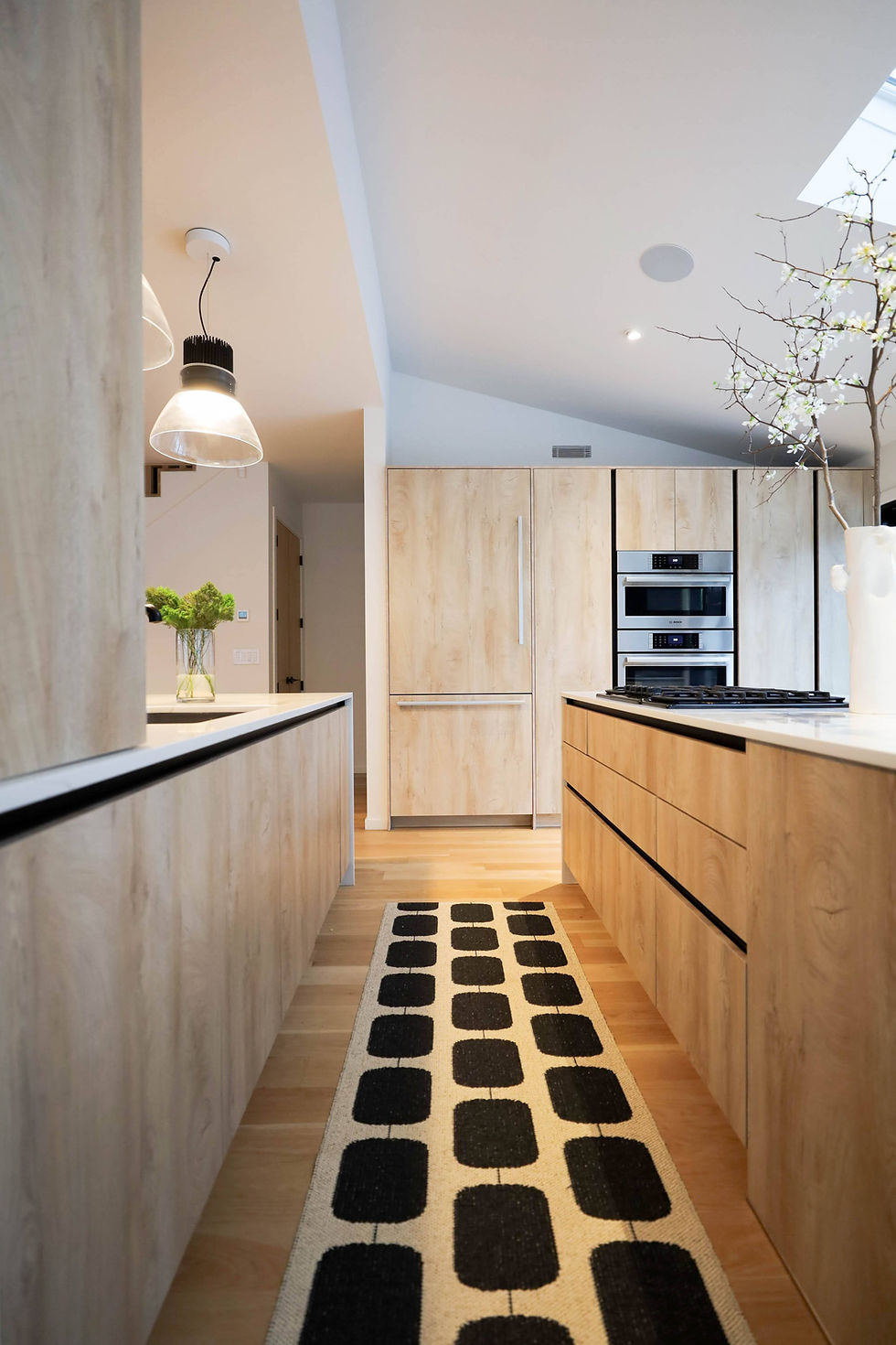Open-concept family kitchen in Long Island with two island work zones, handleless wood-look cabinetry, specialized pantry storage, and design features that contributed to an $81K kitchen investment.