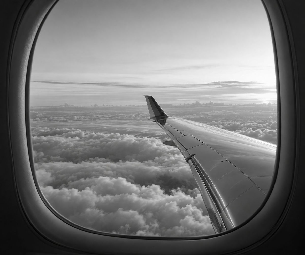 View of a wing above the clouds through an aircraft window