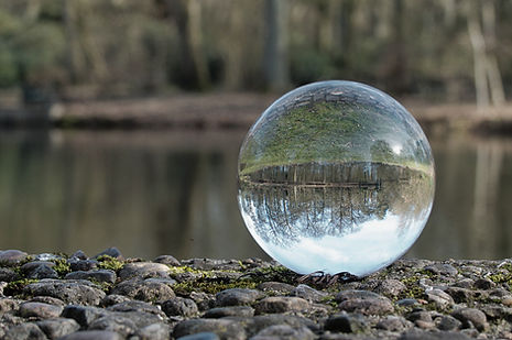 Clear crystal ball on moss covered rocks reflecting water and green trees