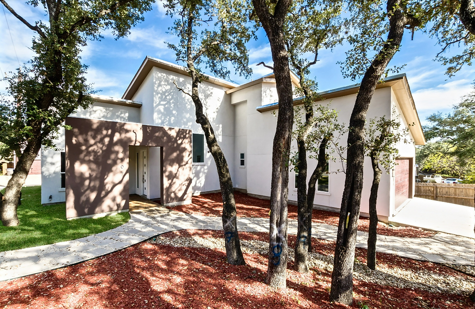 Modern single-story home with a bright white exterior and clean lines, surrounded by mature oak trees and red mulch landscaping.