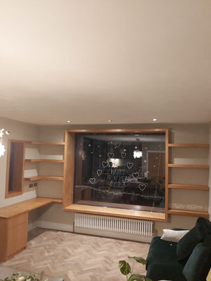  Custom-built wood desk with shelving and a cozy nook seating bench around a window, designed to maximise space and functionality in a stylish, organised setting.