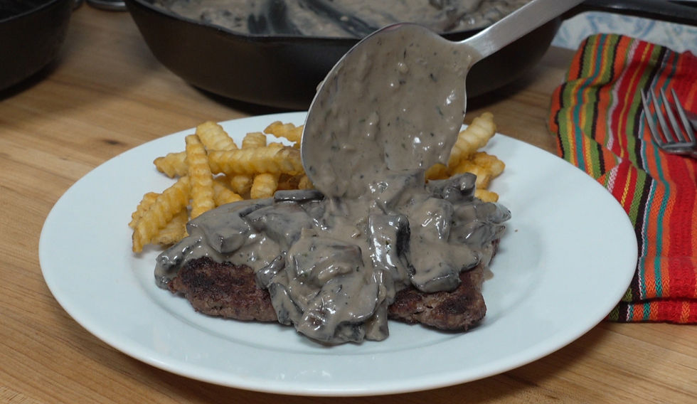 A serving of creamy mushroom gravy is generously spooned over a hearty hamburger steak, accompanied by crispy crinkle-cut fries.