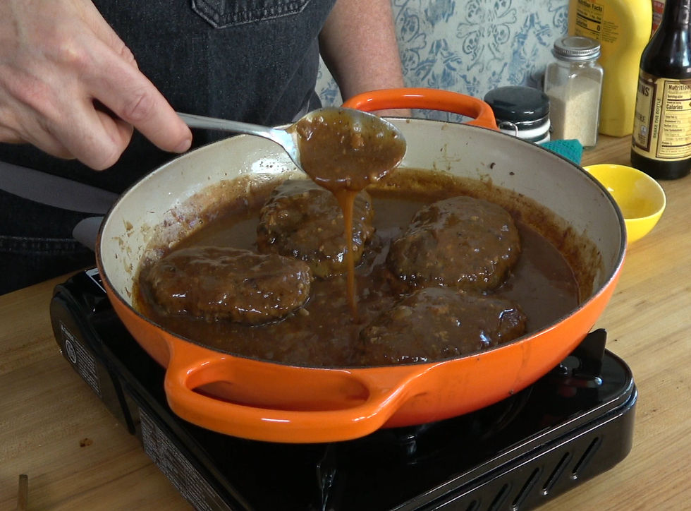 Classic Salisbury steak simmers in a rich, homemade brown gravy in a vibrant orange pan, ready to be served for a comforting meal.