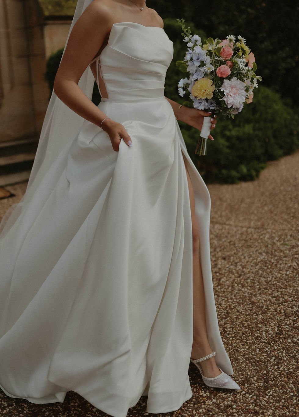 A stunning Bride in a bridal gown carrying her Bloom Illusions Garden Style Bouquet in pastel colours as she walks down a pathway.