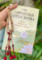 A close up of person holding the Threefold Lotus Sutra book with beads in hand.