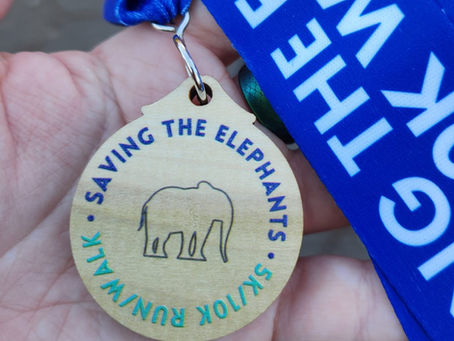 Photograph of Christine's hand holding a wooden medal depicting an elephant outline. Its text reads Saving the Elephants 5k/10k run/walk
