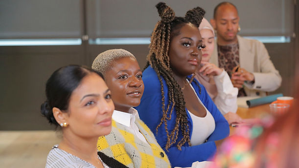 A non-binary person sitting at a conference table with their colleagues