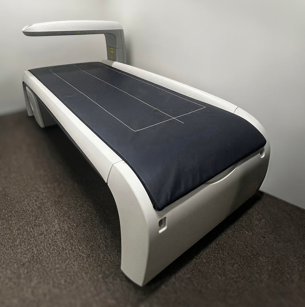 A white x ray bed with a blue cushion, sitting in the corner of a room