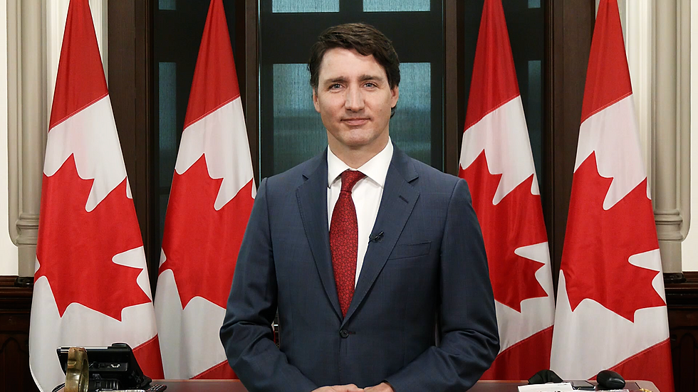 Highlight video in event - Person in a suit stands before Canadian flags, with a neutral expression. Dark background and red tie add to formal setting.