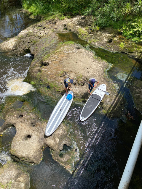 Two people carrying TAKACAT inflatable SUPs in a river, showcasing innovative and durable water sport products designed for outdoor adventures.