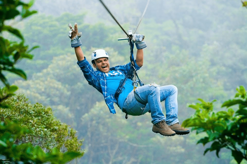 Hombre deslizándose en tirolesa por el bosque tropical.