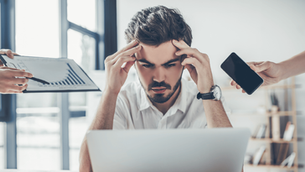 Stressed executive at laptop surrounded by distractions — smartphone, reports, and notifications — symbolizing split attention and cognitive overload.