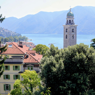 View over the rooftops of a city towards a lake and a mountain panorama with a church tower in the foreground.