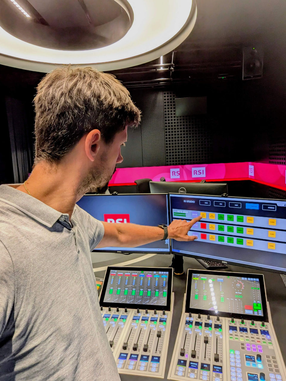 Person zeigt auf einen Monitor mit einer rasterförmigen Übersicht von Audio‑Kanälen in einer digitalen Steuerungsoberfläche.
