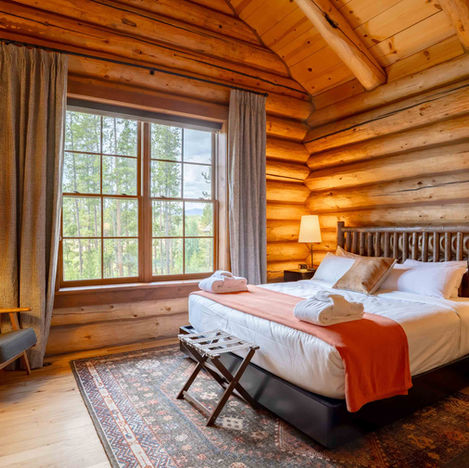 Warm log cabin bedroom interior with king bed, rustic wood walls and forest window view – Colorado lodge photography by Alex Miller