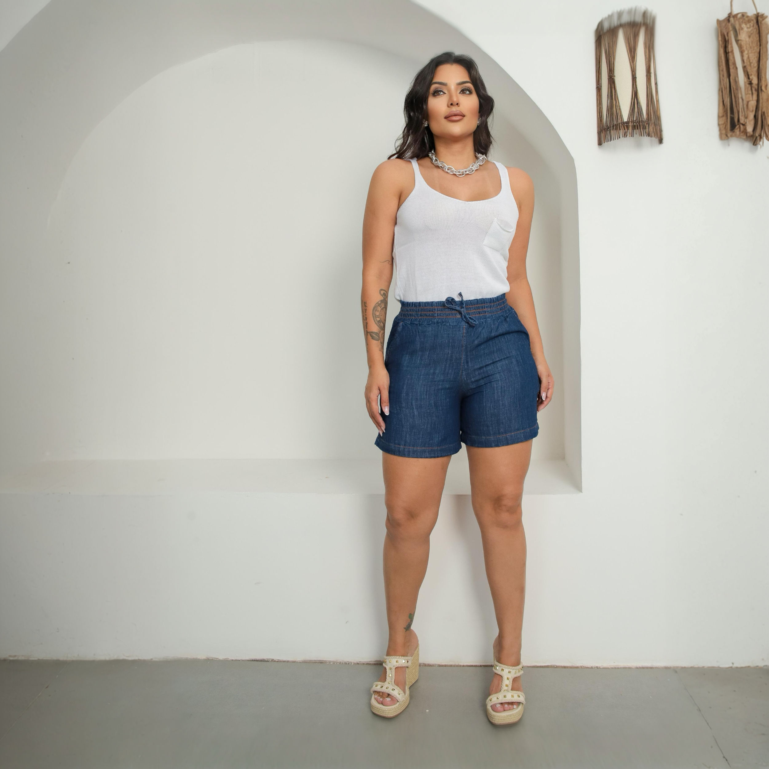 Mulher vestindo short jeans feminino azul e regata branca.