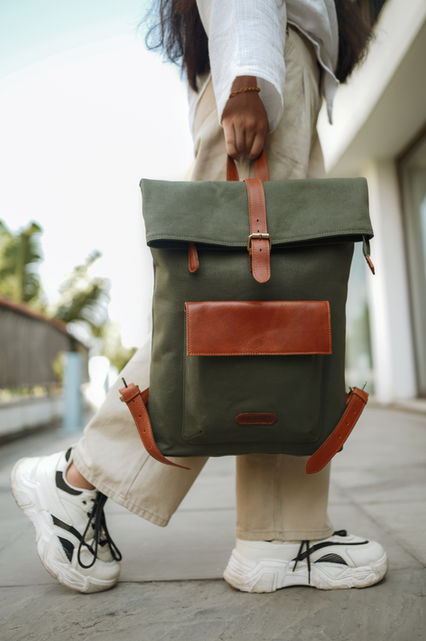 Person holding green backpack with brown accents; outdoor setting; Vintanaro.