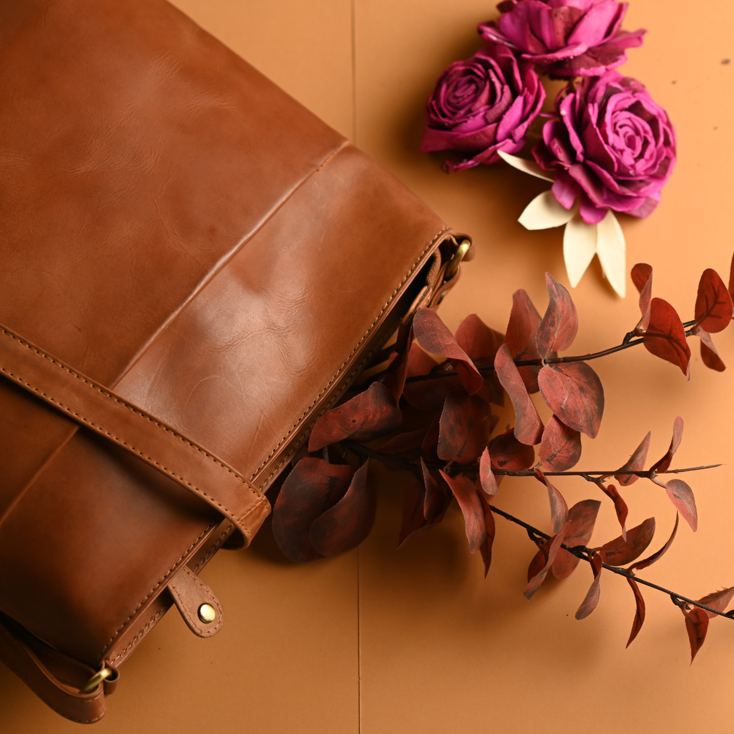 Brown leather bag with flowers and leaves on a brown background.