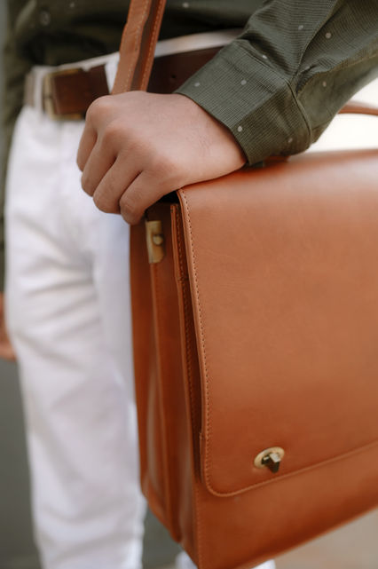Man holds a brown leather bag, wearing white pants and a green shirt.