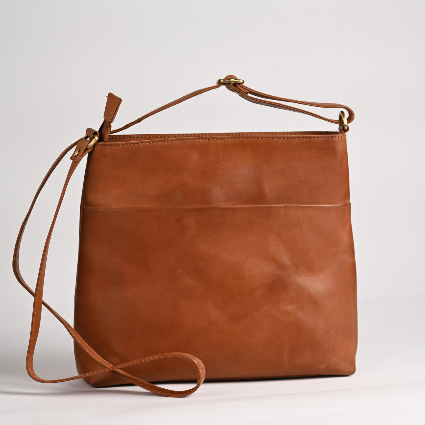 Brown leather shoulder bag with long strap and single pocket for carrying.