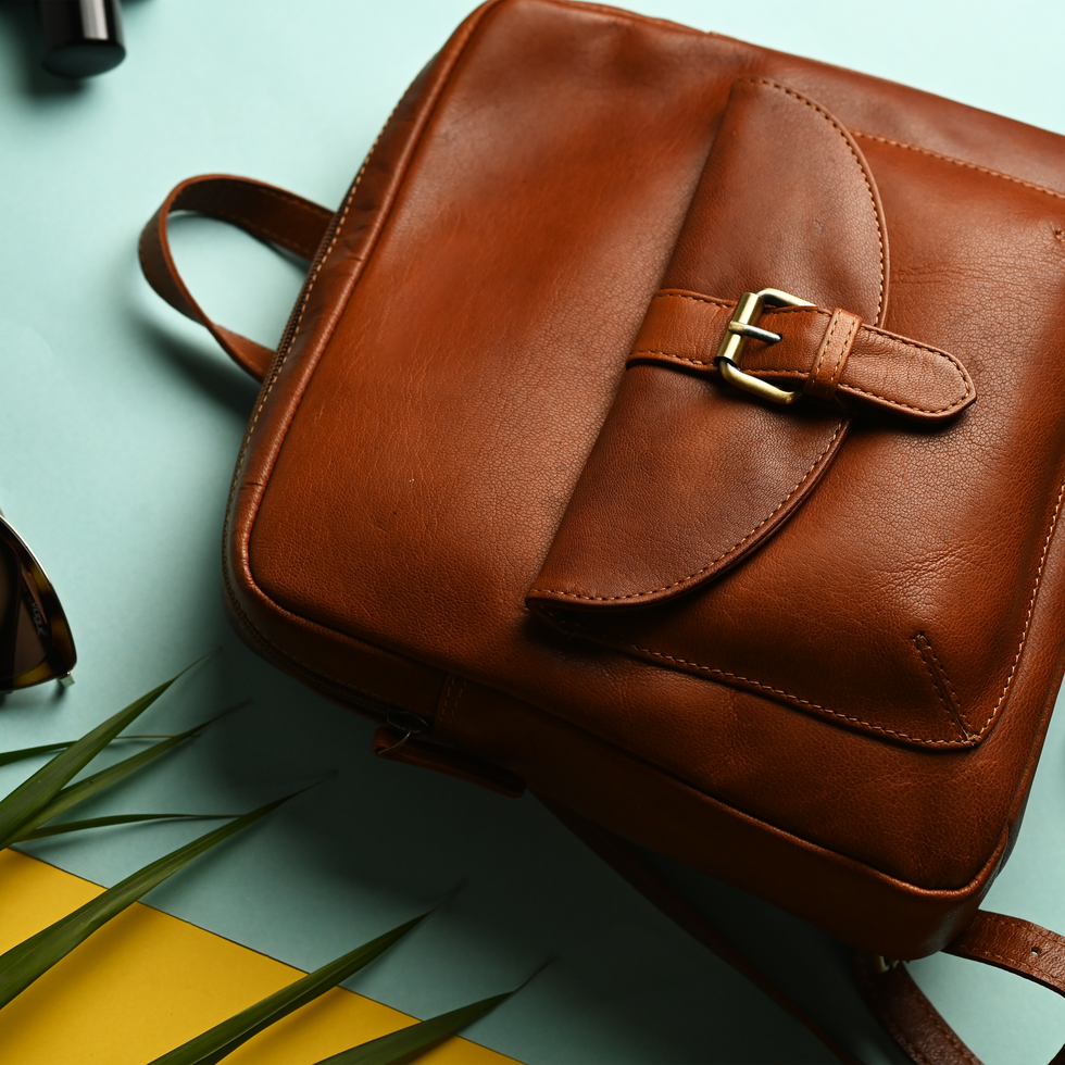 Brown leather backpack, gold buckle, sunglasses. Stylish bag on colorful background.