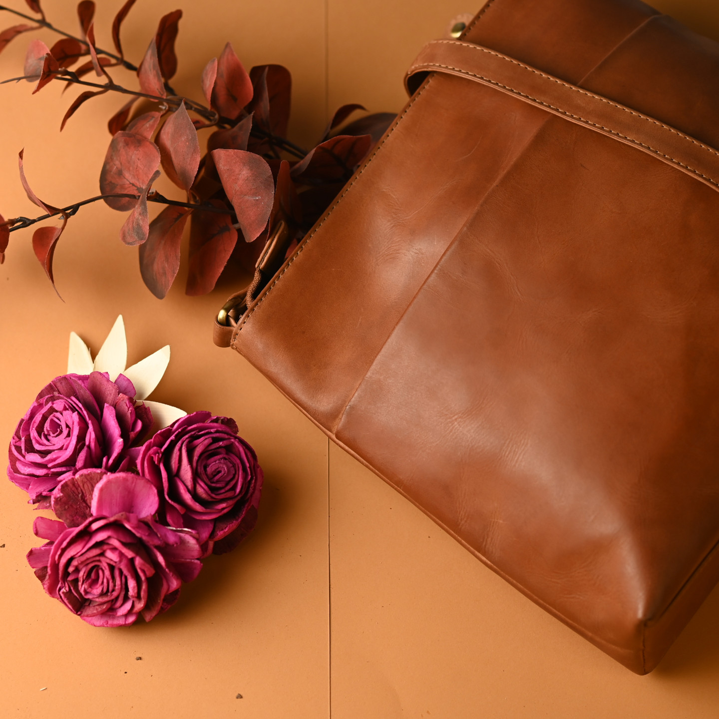 Brown leather bag beside artificial flowers on a warm brown surface