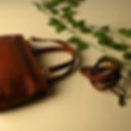 Brown leather bag with strap and decorative leaves on white surface.