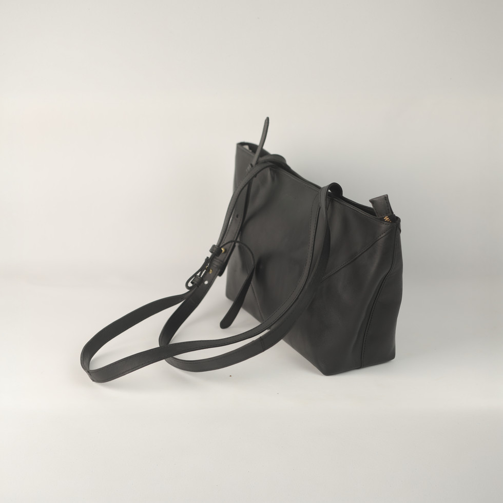 Black leather bag with long strap, background is plain white. Feather Touch Impex Pvt. Ltd.