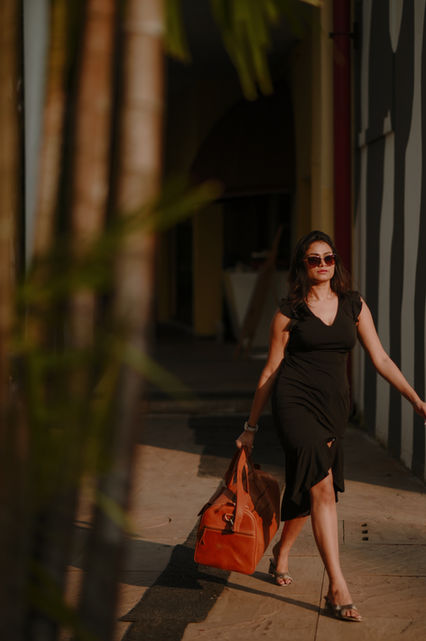 Woman in black dress walking with orange bag on sunny street.