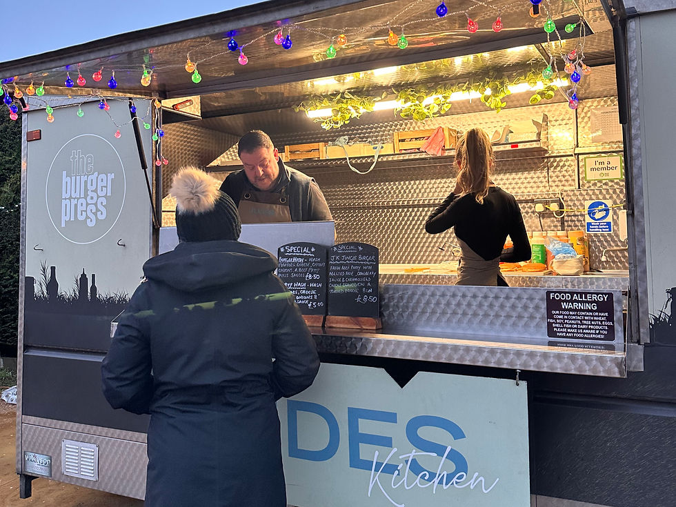 Person at food truck counter under colorful lights. Vendor prepares order. Chalkboard menu displays specials. Moody evening ambiance.