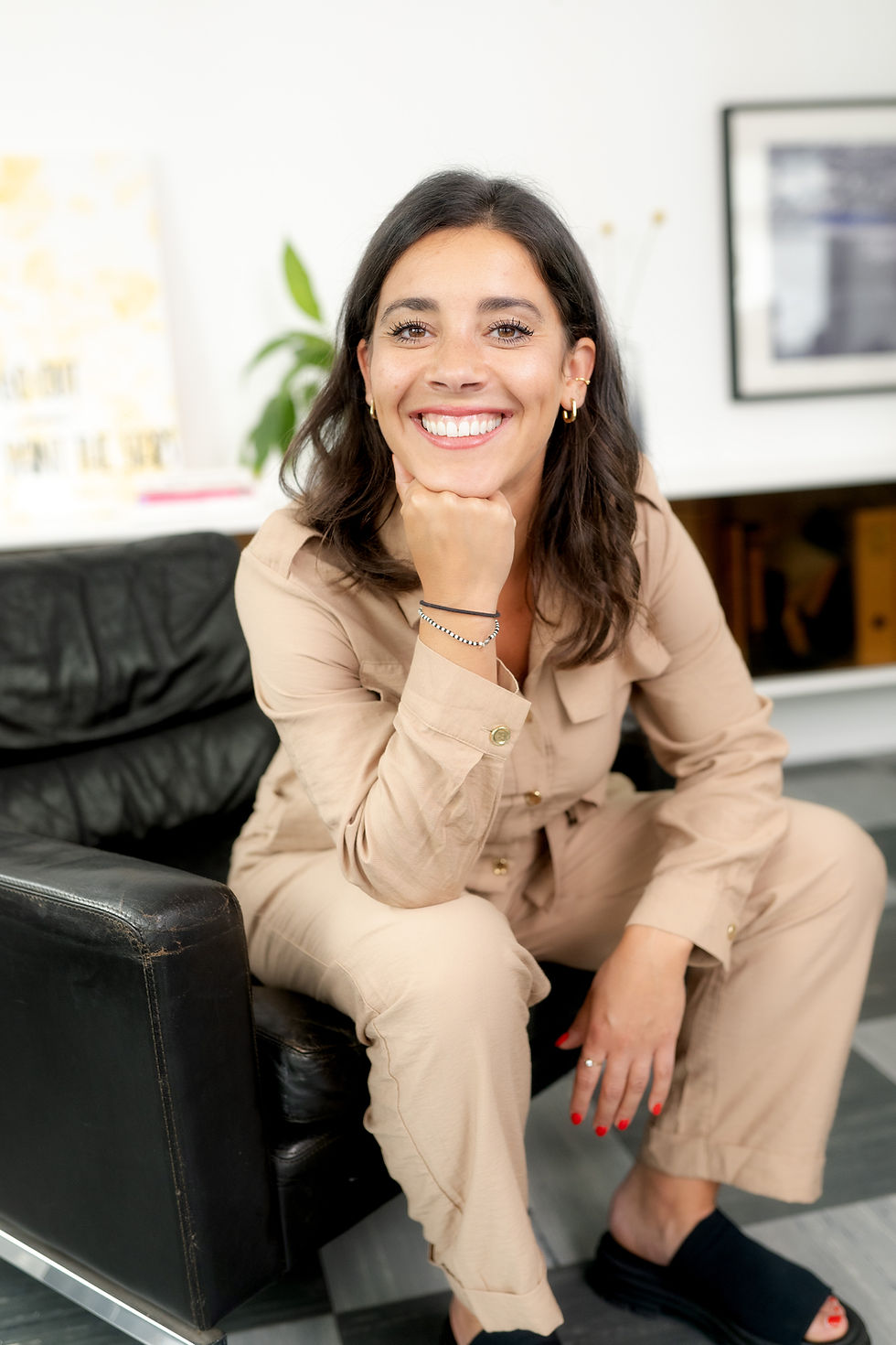 Frau im beigen Overall auf Sofa, lächelnd mit Blick zur Kamera