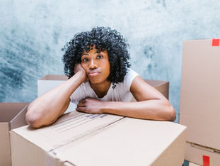 Tired mom leaning on a moving box, head resting on her hand, surrounded by packed cardboard boxes.