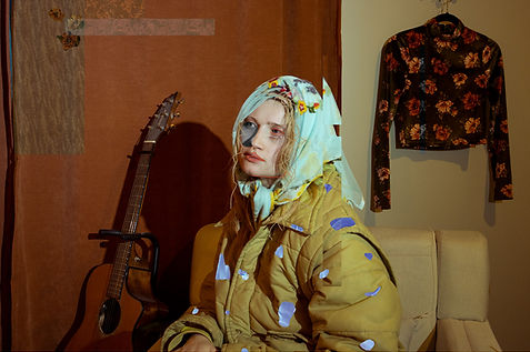 A portrait of a girl sitting in a chair with a blue sweater around her head.