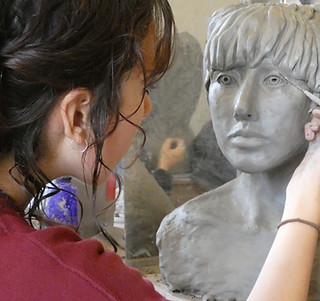 A teenage high school student in a red shirt with dark hair at Summerfield Waldorf School is working on her self portrait sculpture project for art class.