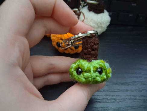 A green crochet amigurumi pumpkin keychain.