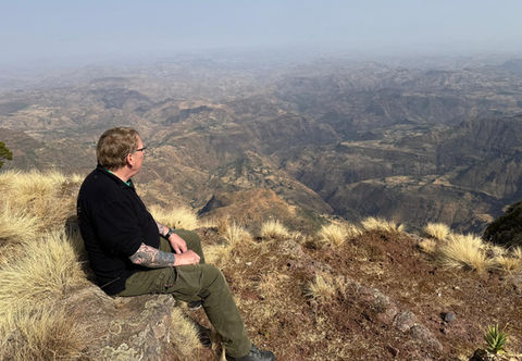 Mann sitz an Bergkante mit Panoramablick