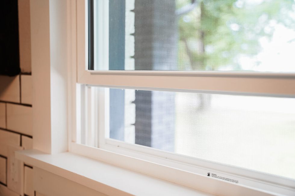 A close-up view of a white residential window frame and screen being inspected for tears or damage to keep summer bugs out of a Kansas City home.