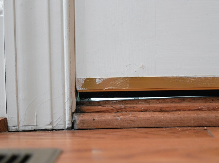 A worn door sweep at the bottom of an exterior door showing a gap with daylight shining through, a common entry point for pests.